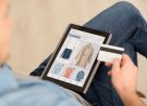 Pay it off. Pleasant man sitting on the couch and holding credit card while using tablet
