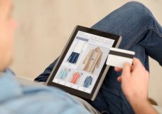 Pay it off. Pleasant man sitting on the couch and holding credit card while using tablet