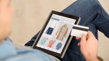 Pay it off. Pleasant man sitting on the couch and holding credit card while using tablet