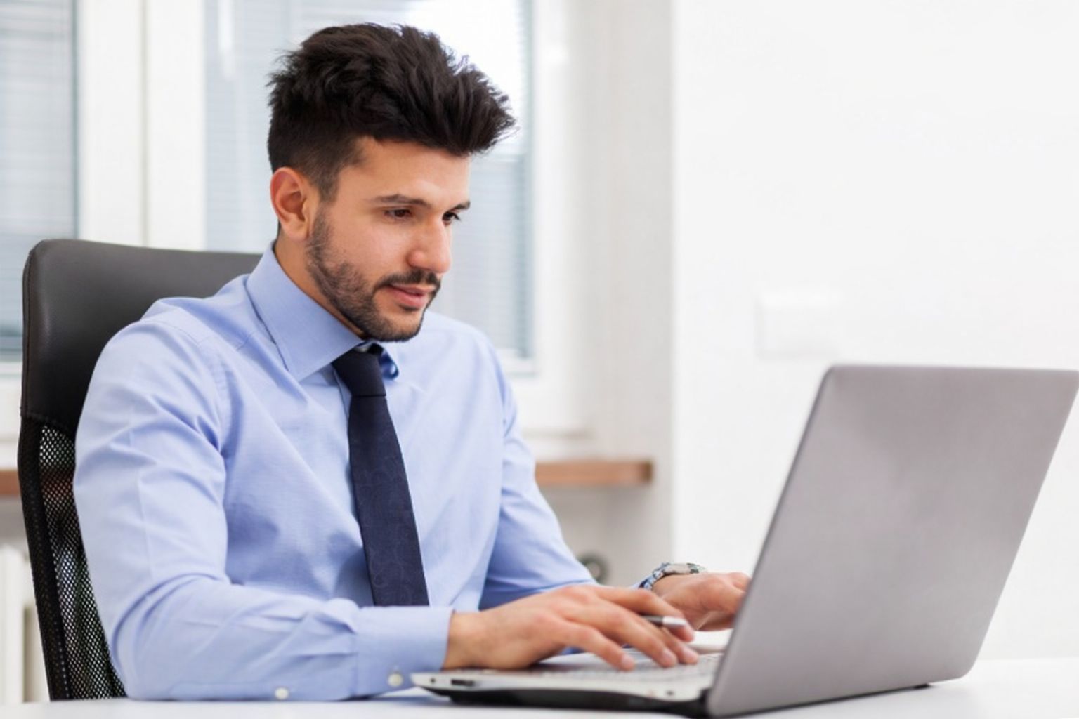 Mies työskentelee kannettavalla tietokoneella toimistossa, keskittyneenä taloushallintoon.